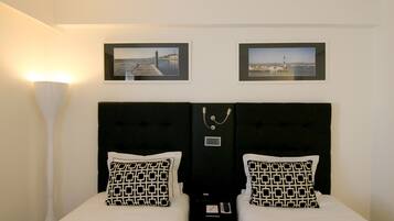 Quarto de hotel com duas camas, cabeceira com painel de controle e duas imagens emolduradas na parede.