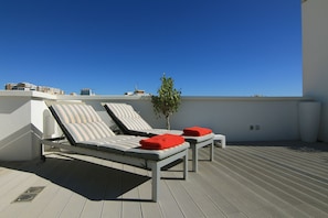 Terraço no telhado com duas cadeiras de descanso, uma pequena planta em vaso e um céu azul límpido.