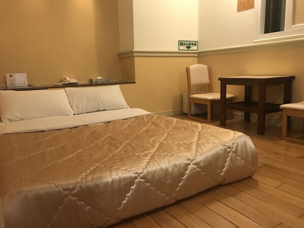 A hotel room with a large bed, a chair, a small table, and a window. - Good Hotel (Taichung)