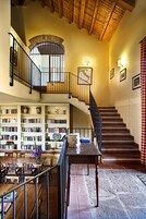 Una biblioteca amplia con estanterías, una escalera de madera y un comedor con mesas y sillas.