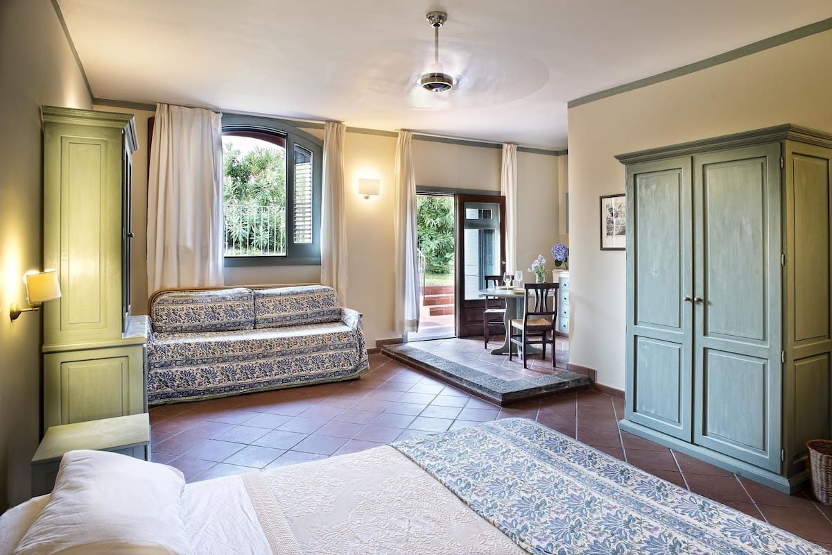A bedroom with a bed, a sofa, a wardrobe, and a view of the outside.