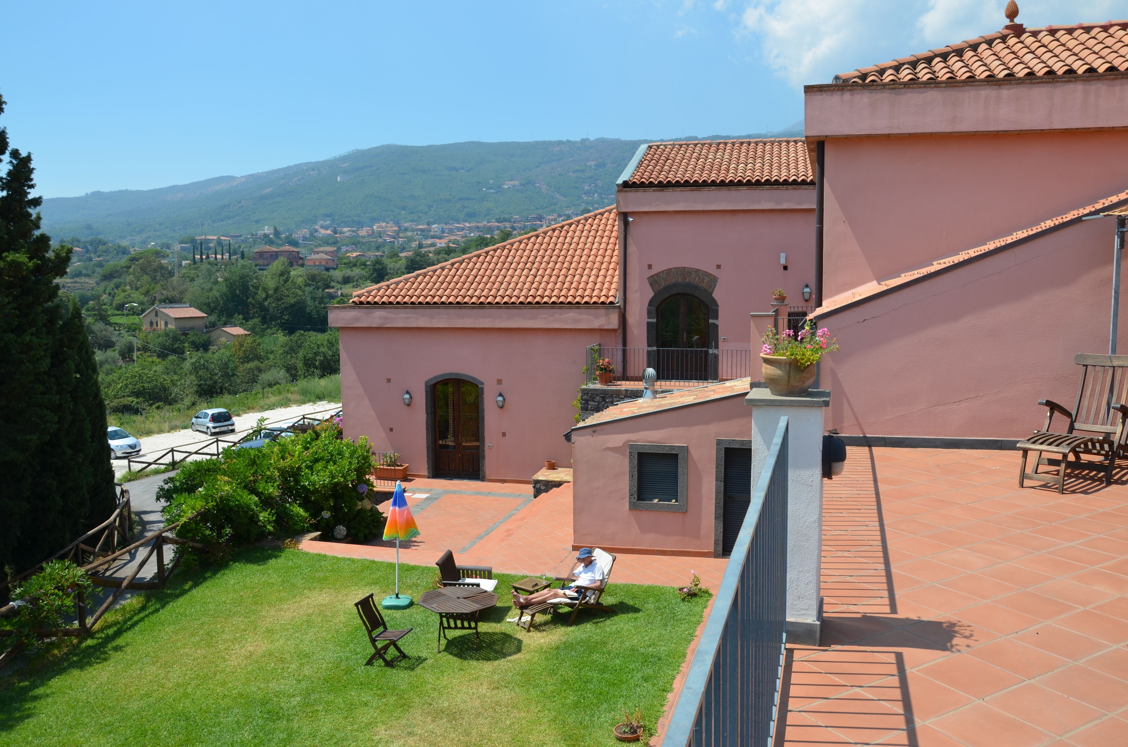 Une villa rose avec un toit en tuiles, un patio avec une table et des chaises, et une vue sur le paysage environnant.