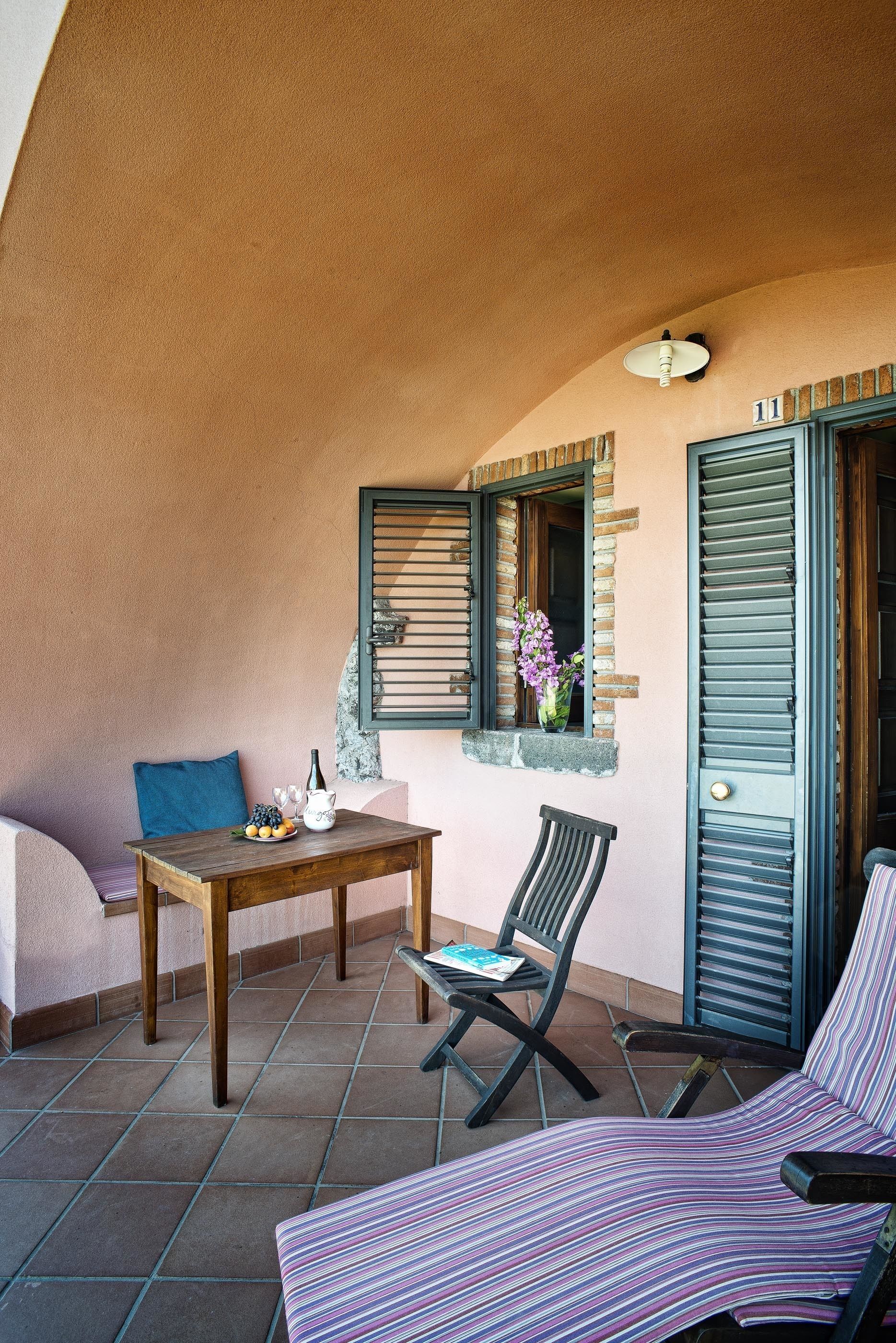 Un patio acogedor con una mesa de madera, una silla lounge a rayas y un banco acolchado.