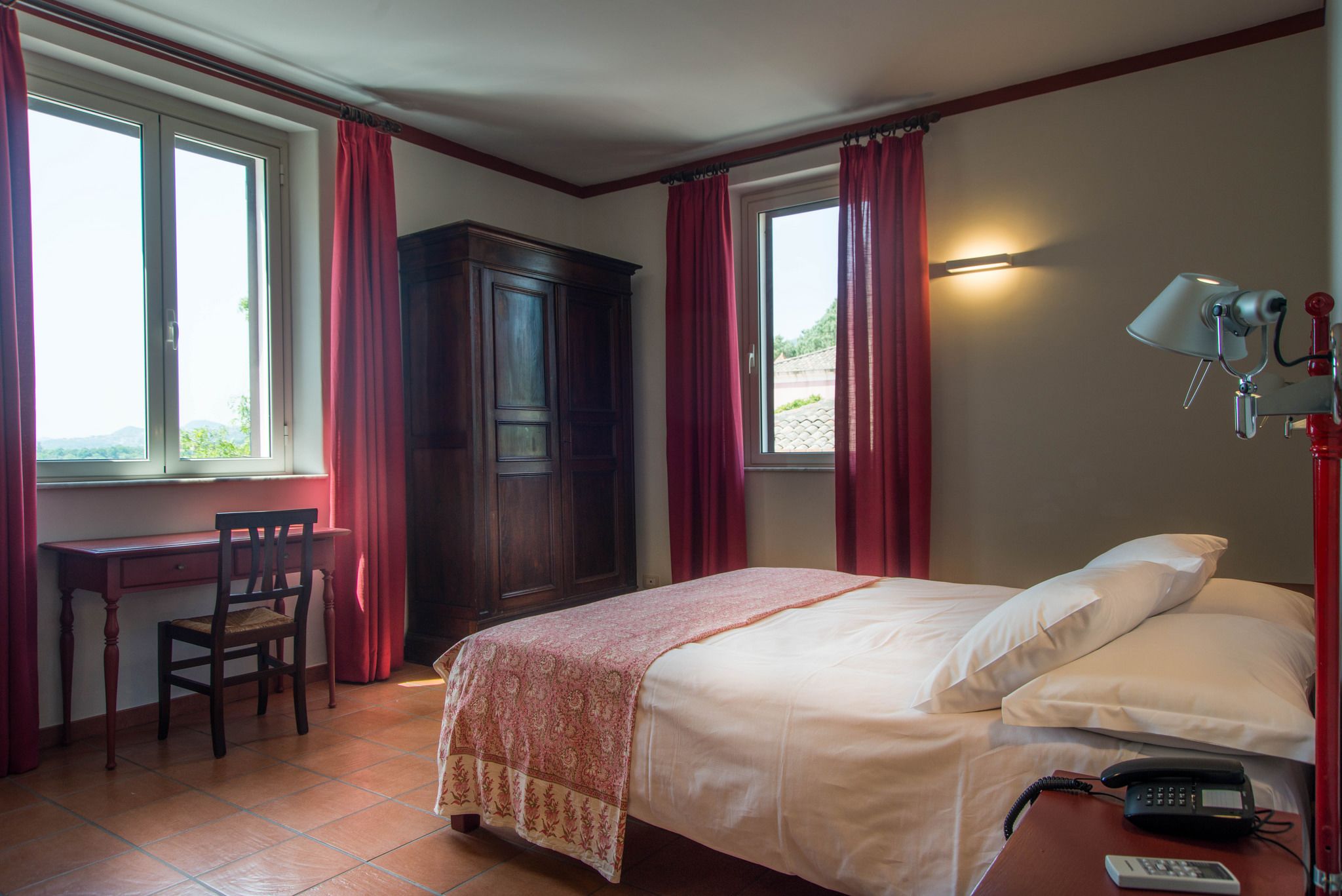 A hotel room with a bed, a desk, a chair, a wardrobe, and a telephone.