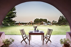 Un patio con mesa y sillas, vista a un área verde y cielo despejado.