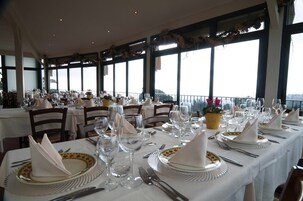 Un restaurante con varias mesas preparadas para comer, con manteles blancos y vajilla, copas y cubiertos dispuestos ordenadamente.
