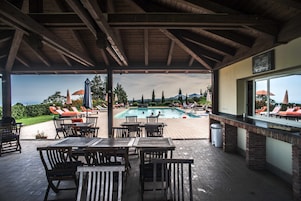 Un patio al aire libre con mesas y sillas de madera, una piscina y sillones de descanso.