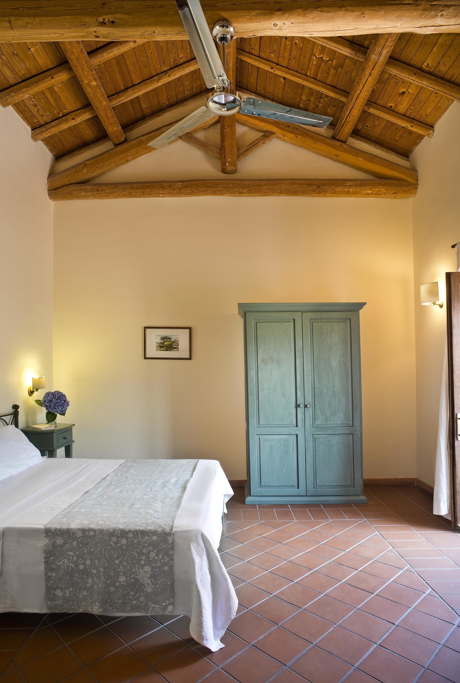 Een slaapkamer met een houten plafond, een bed, een blauwe garderobe en een wandlamp.