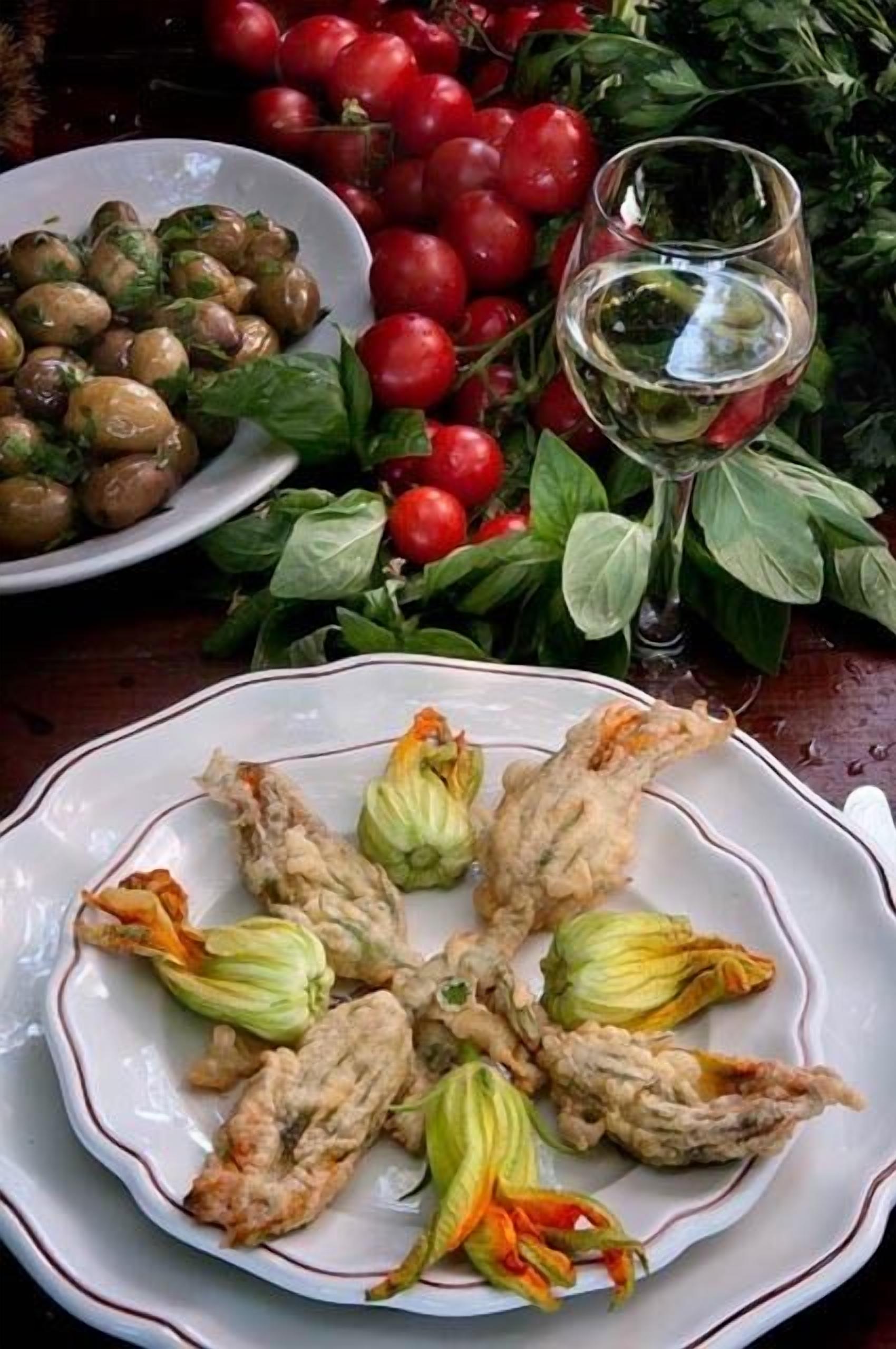 Une assiette de légumes frits et un verre de vin blanc sur une table, avec des tomates fraîches et du basilic.
