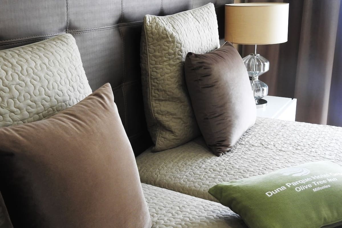 A bed with a quilted headboard, multiple pillows, and a green pillow with text.
