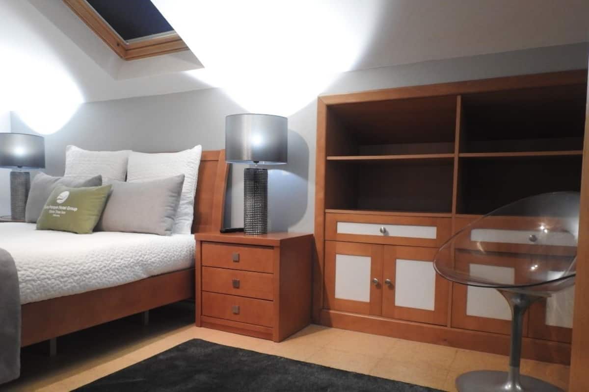 A bedroom with a bed, bedside lamps, a nightstand, a wardrobe, and a glass table.