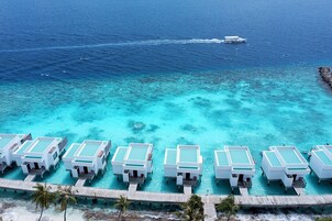 A resort with overwater bungalows, clear turquoise waters, and a boat in the distance.