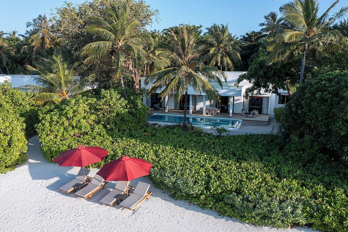 A beachfront property with a pool, palm trees, and a white building.