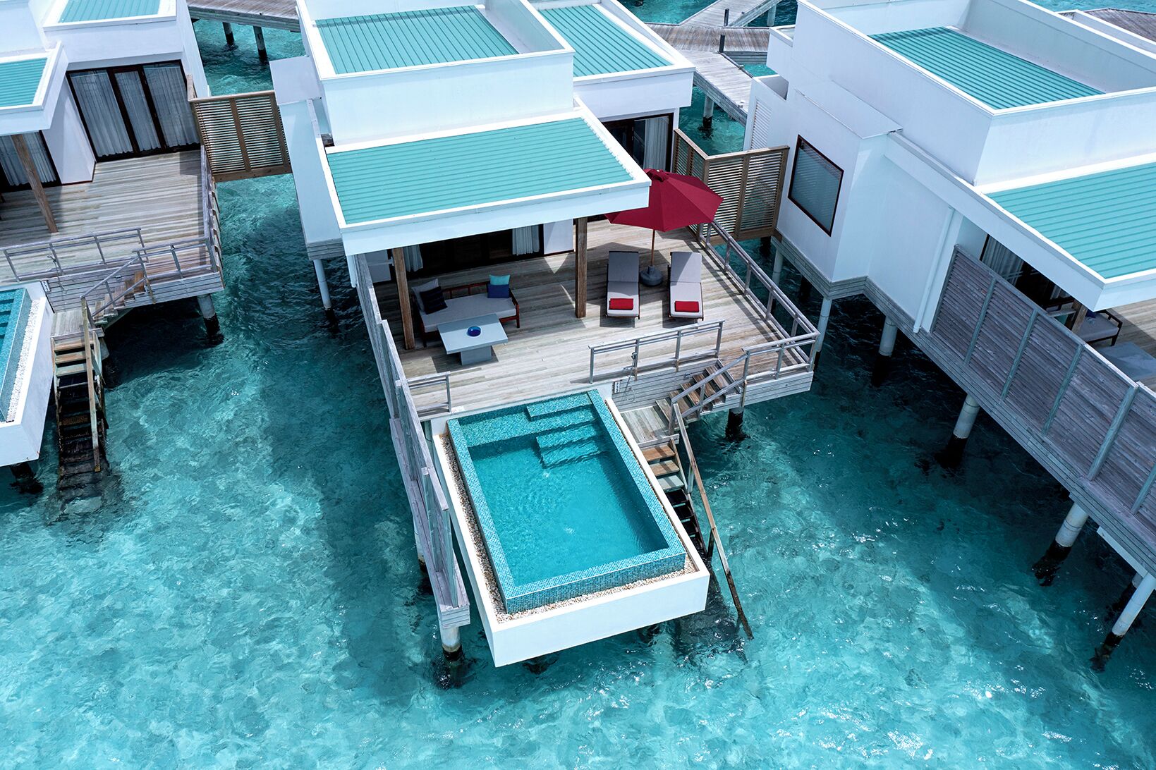 An overwater bungalows with a central pool, wooden deck, and lounge area.