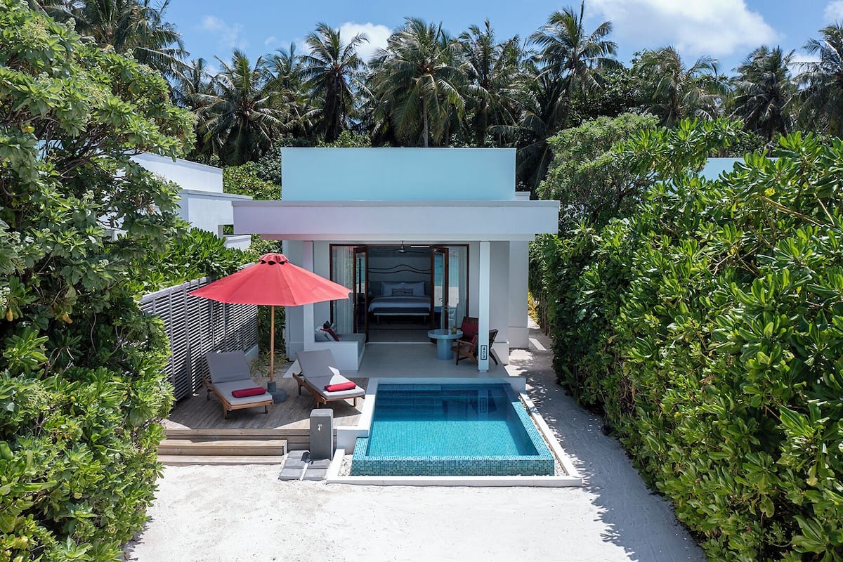 A modern resort with a private pool, lounge area, and a bedroom visible through an open door.