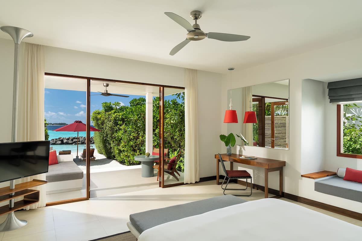 A modern hotel room with a large bed, a desk, and a view of the ocean.