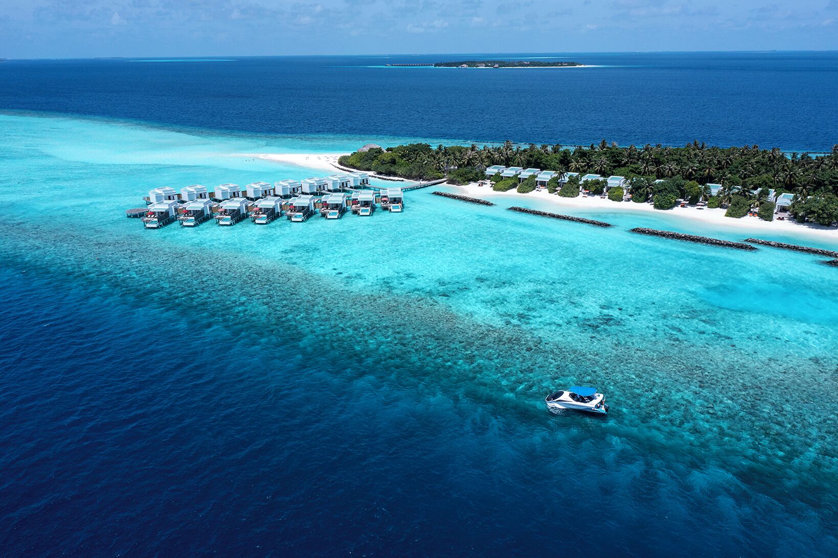 Vista aérea de un complejo turístico con bungalows sobre el agua, una playa y un mar azul cristalino.
