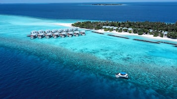 Vista aérea de un complejo turístico con bungalows sobre el agua, una playa y un mar azul cristalino.