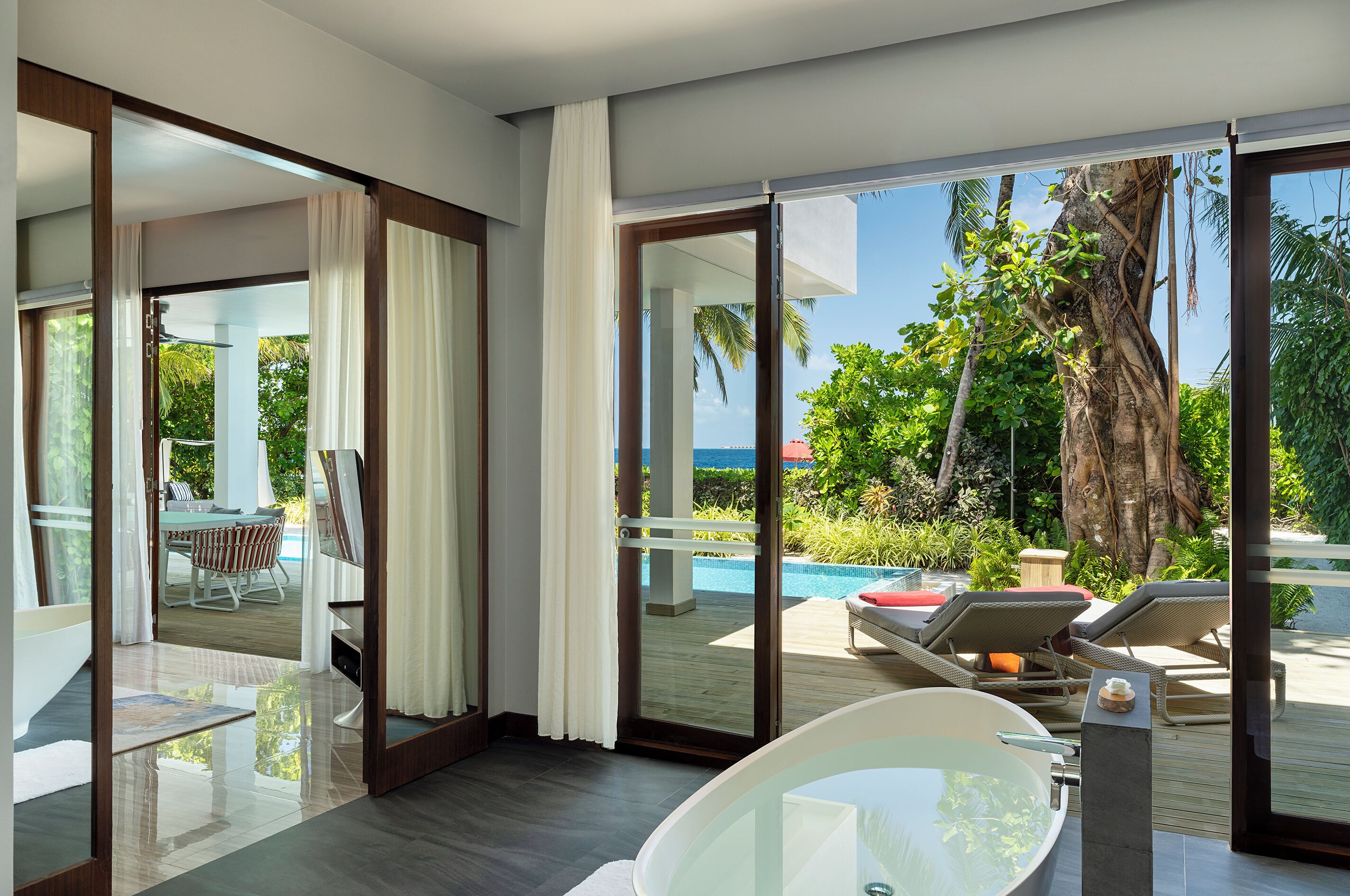 Quarto de hotel moderno com uma grande porta de vidro que dá para uma área de piscina, um espaço de refeições privativo e uma banheira grande.
