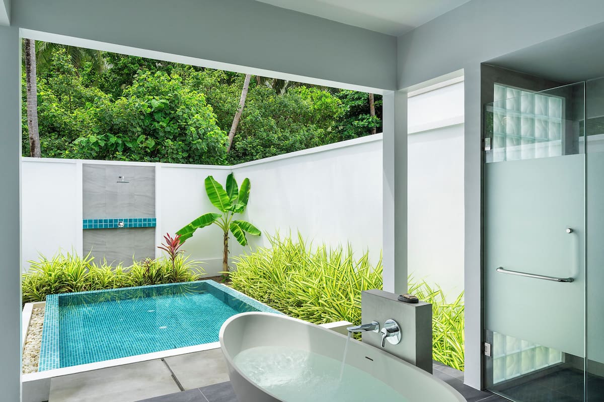 A modern bathroom with a freestanding bathtub, a glass shower enclosure, and a small pool area with tropical plants.