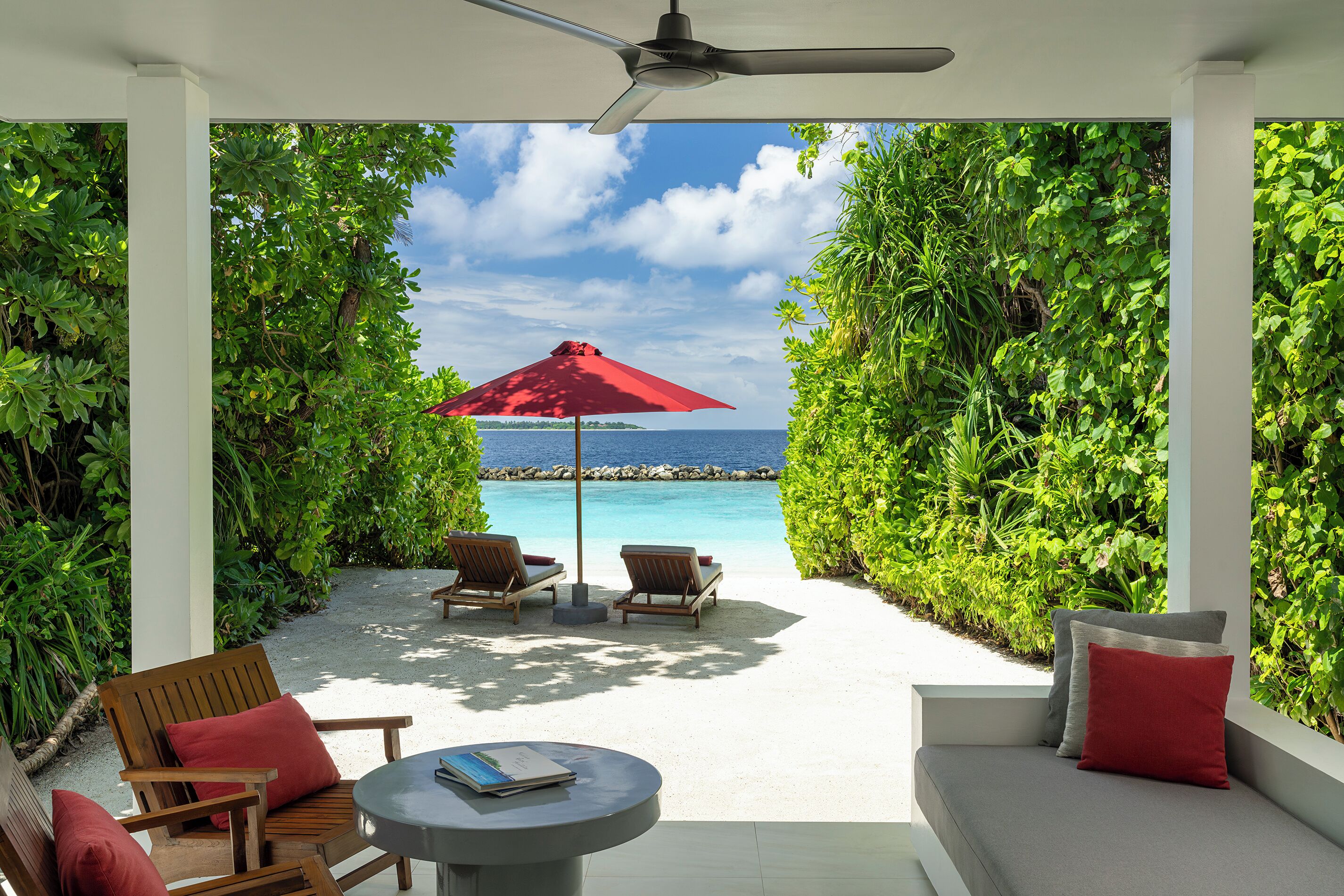 A patio with a view of the ocean, featuring a red umbrella, two lounge chairs, and a small table.
