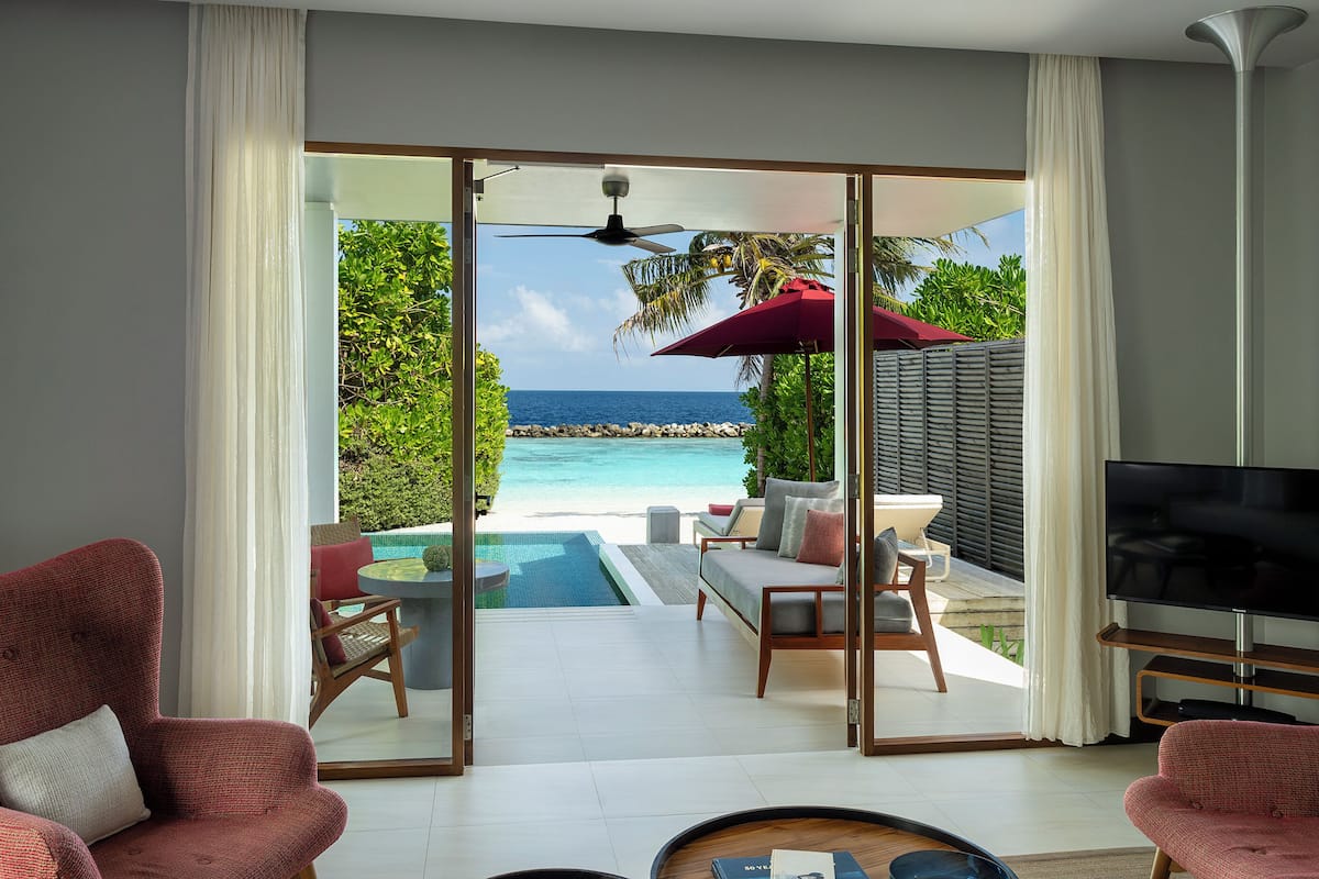 A living room with a large sliding glass door leading to a pool and a view of the ocean.
