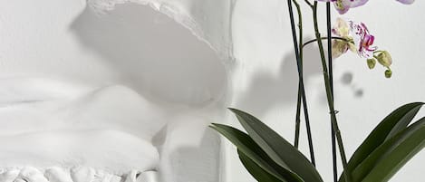 A bed with white bedding, a decorative pillow, and a potted orchid plant on a white nightstand.