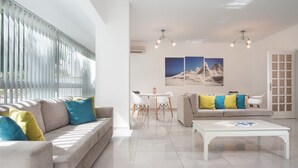 A modern living room with a sofa, coffee table, and dining table. - Milos Hotel (Milos)