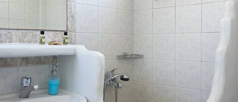 A bathroom with a sink, mirror, shower, and a window.