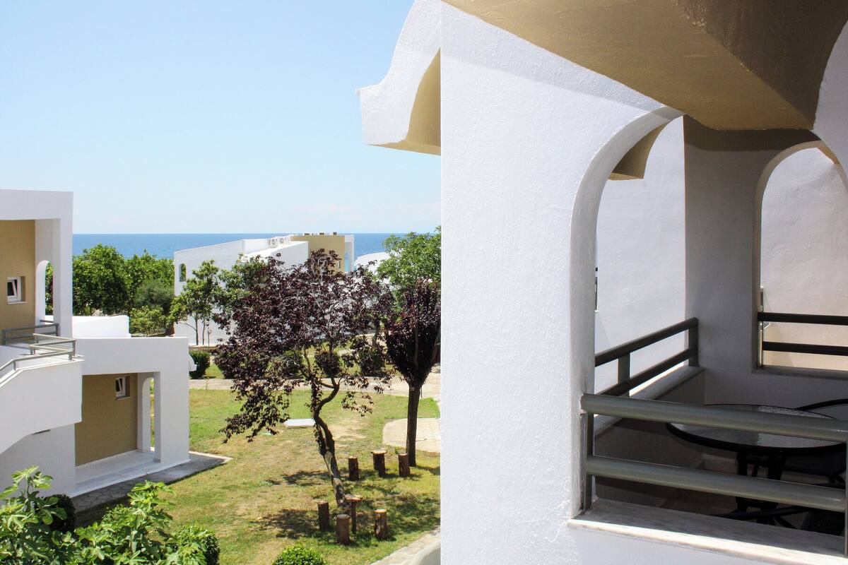 Un bâtiment moderne doté d’un balcon, offrant une vue sur la mer et comprenant un jardin avec des arbres.