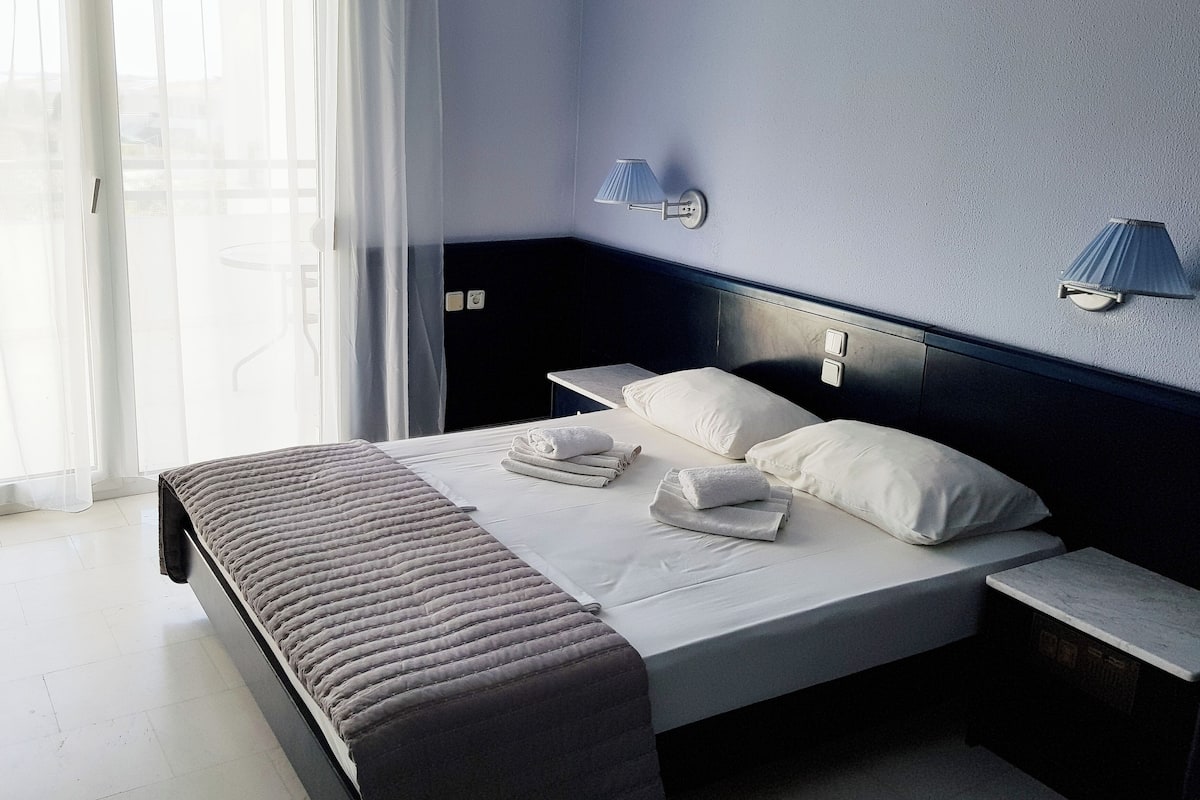 Un lit bien fait, avec des oreillers et des serviettes, une table de chevet et une lampe fixée au mur.