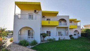 A multi-story building with balconies, a stone pathway, and a well-maintained lawn. - Kamaria Apartments (Hersonissos)