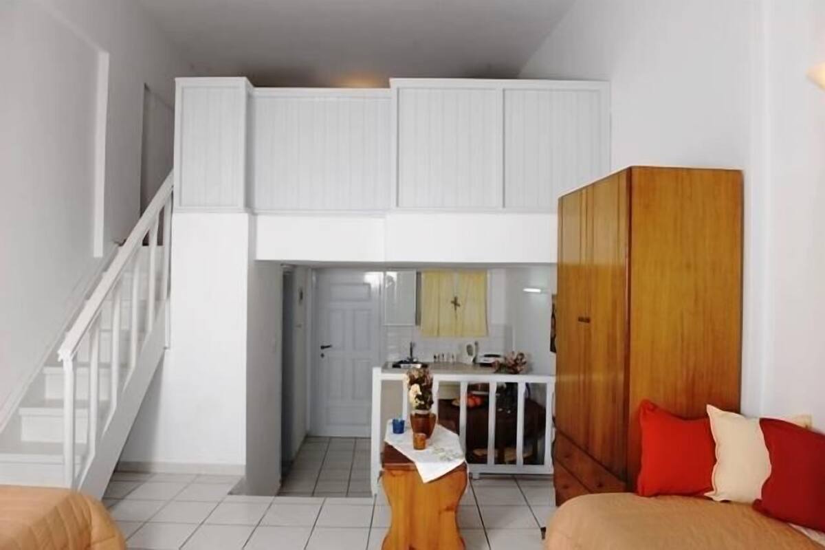 A compact living space with a kitchenette, a wooden wardrobe, and a staircase leading to an upper level.