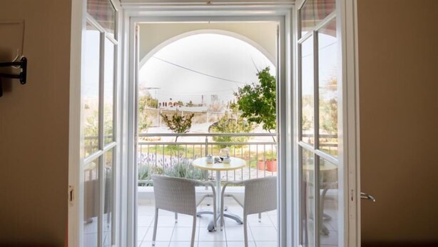 A view from a room with a white door leading to a balcony with a round table and two chairs. - Kamaria Apartments (Hersonissos)