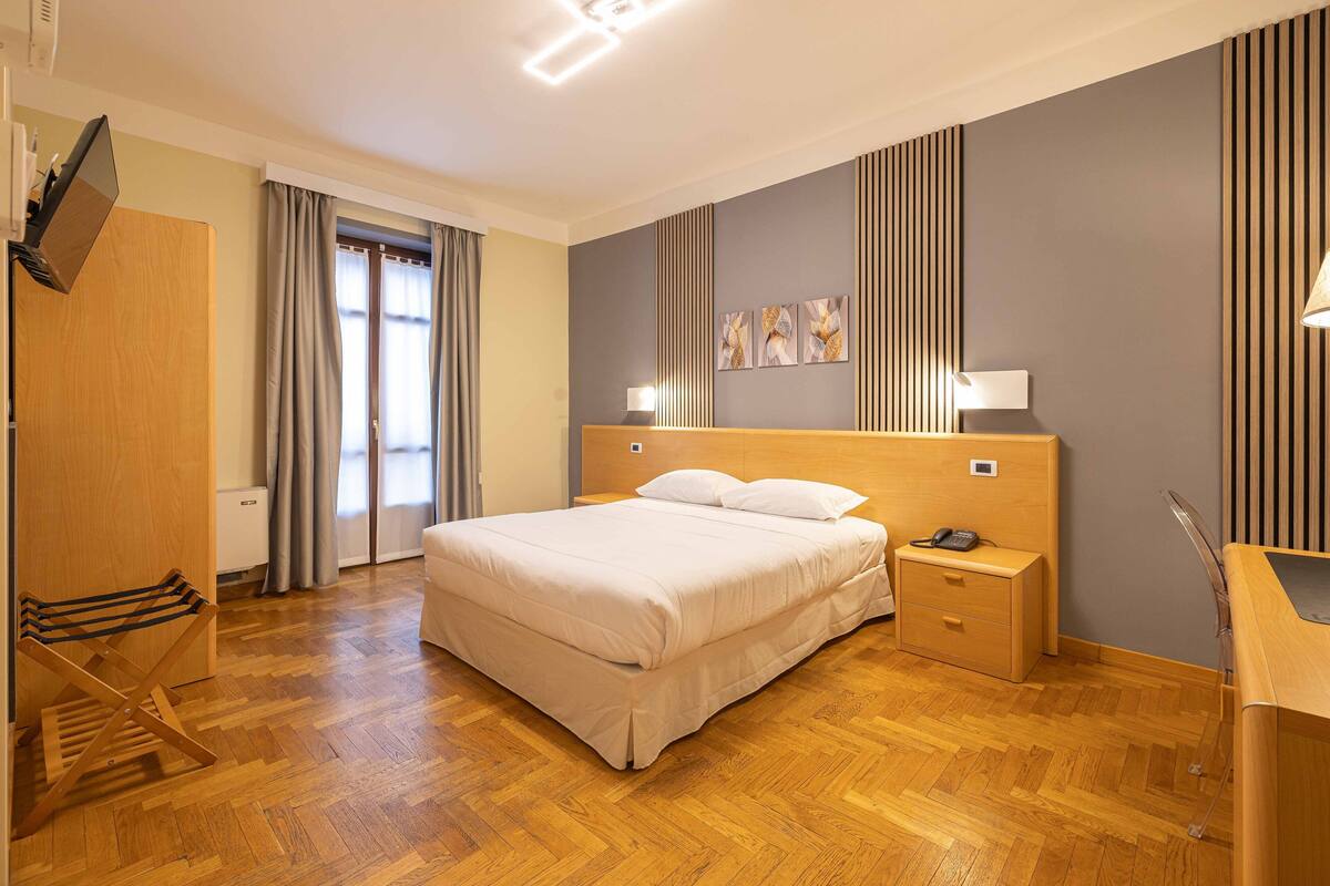 Habitación de hotel con una cama grande, piso de madera, un escritorio con una silla y un televisor montado en la pared.
