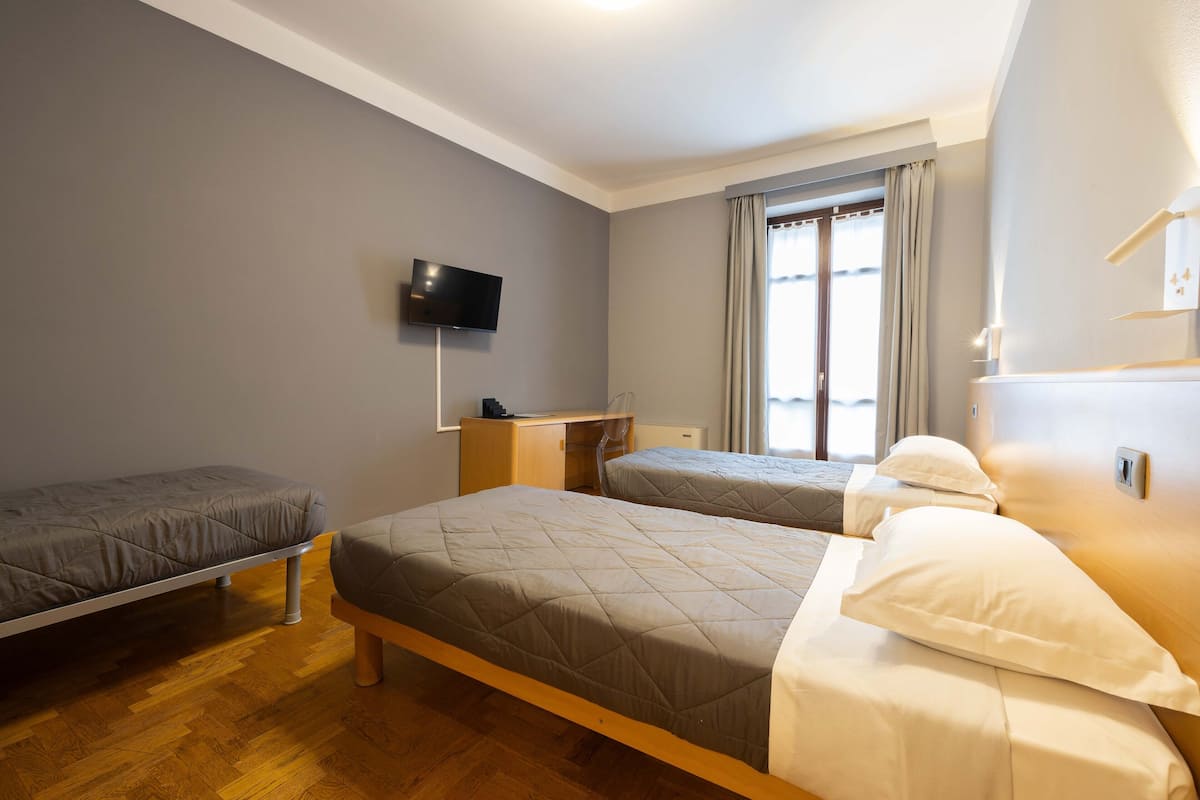 Habitación de hotel con dos camas, un televisor montado en la pared, un escritorio y una ventana con cortinas.