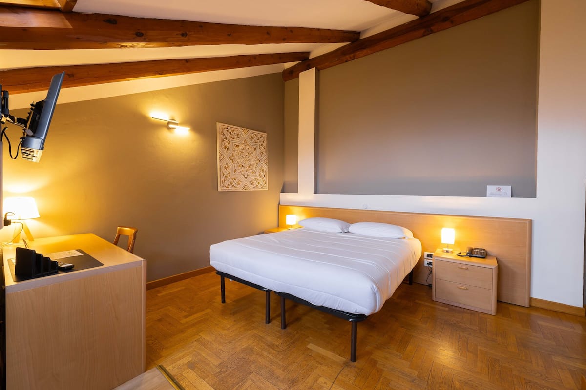 Un dormitorio con cama, mesita de noche, lámpara y un escritorio con silla.