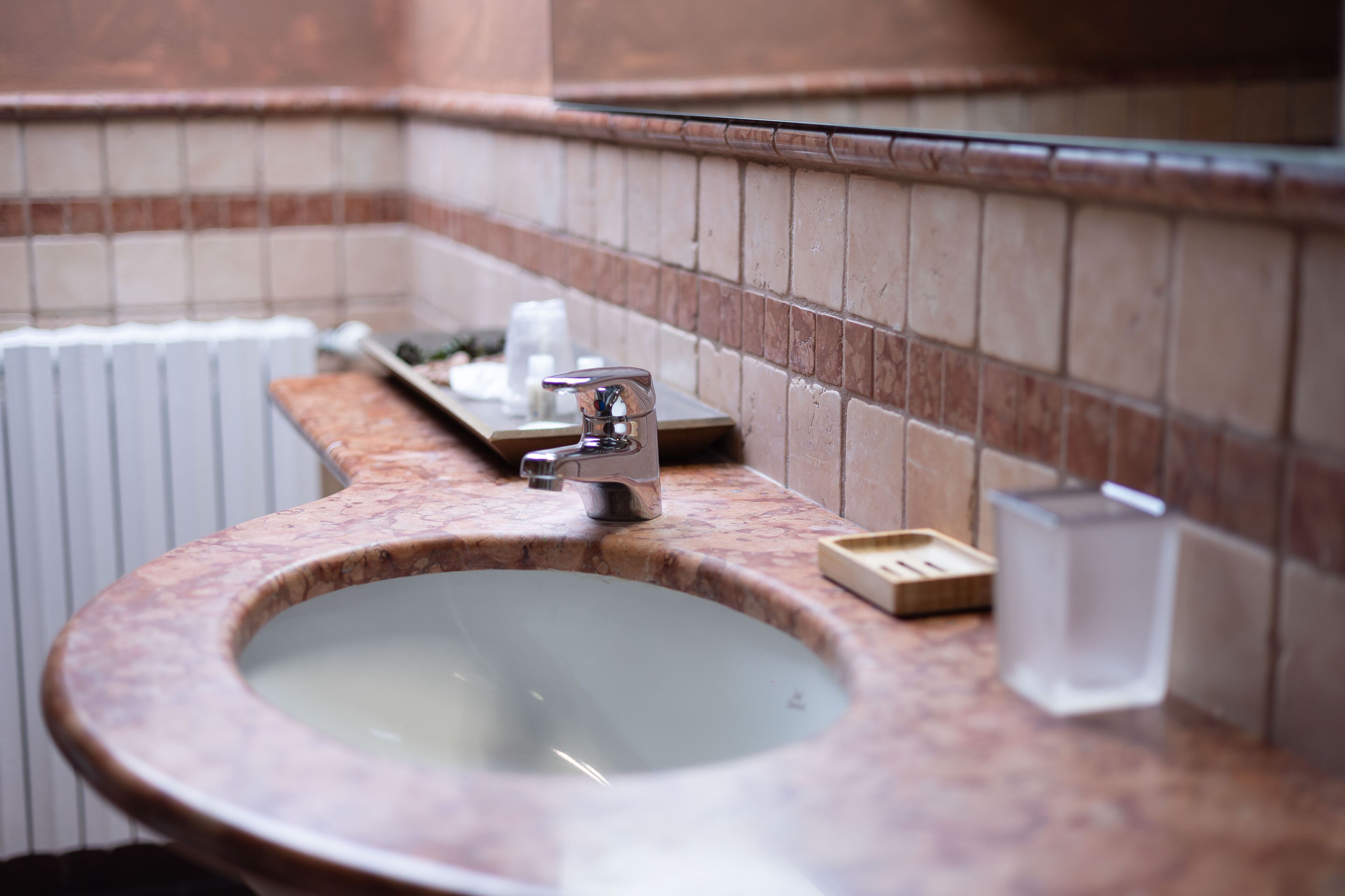 Un baño con lavamanos de mármol, un grifo, un jabonera y un recipiente de vidrio.