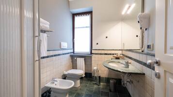 Une salle de bain équipée de toilettes, d’un bidet, d’un lavabo et d’un sèche-cheveux fixé au mur.