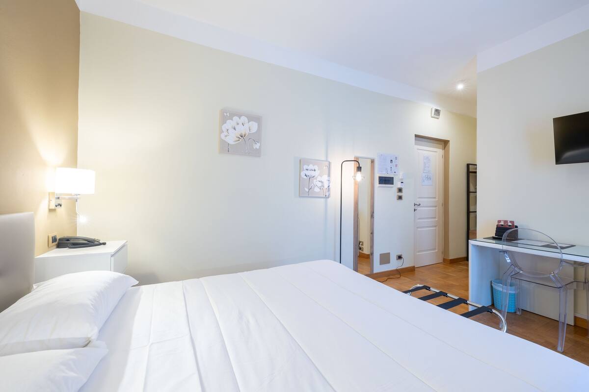 Habitación de hotel con cama, mesita de noche, lámpara, escritorio, silla y televisor montado en la pared.