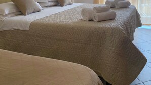 Une chambre d’hôtel avec deux lits, une literie de couleur beige, une tête de lit, un tableau encadré au mur et une fenêtre avec des rideaux.