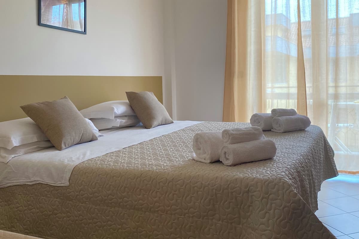 A hotel room with two beds, beige bedding, a headboard, a framed picture on the wall, and a window with curtains.