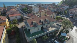 Une ville côtière qui se distingue par un bâtiment remarquable, doté d’une piscine verte, entouré d’autres immeubles résidentiels et avec une marina en arrière-plan.