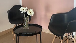 Une pièce avec un mur rose, deux tableaux encadrés, une table noire sur laquelle est posé un vase de fleurs blanches, et deux chaises noires.