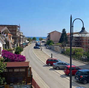 Straßenansicht mit Gebäuden, parkenden Autos und freiem Blick auf das Meer.