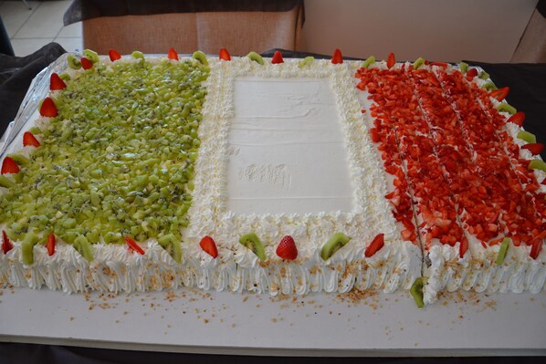 A rectangular cake with three distinct sections, each decorated with different fruits and white frosting. - Hotel Golden (Rimini)