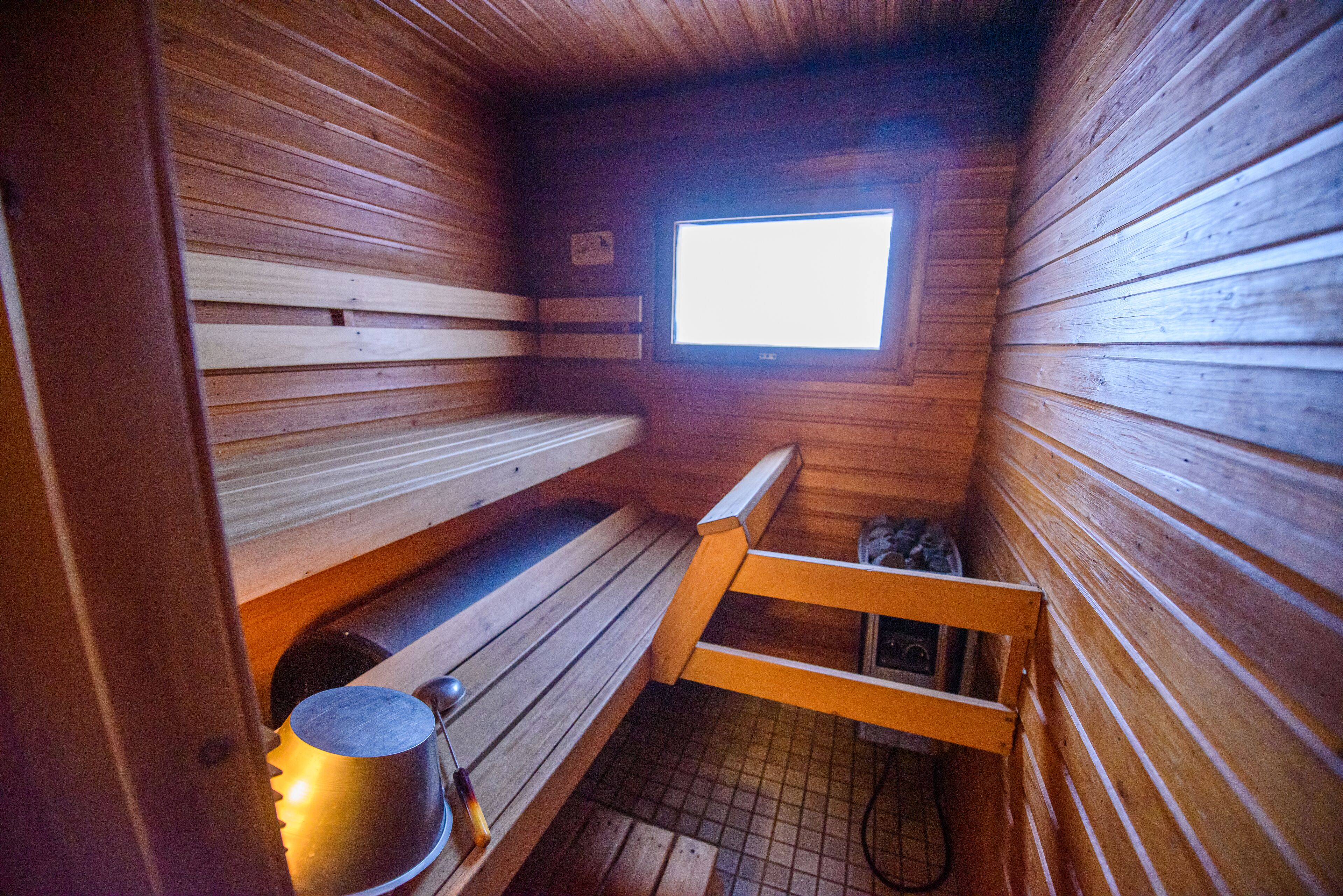 Un sauna avec des bancs en bois, une fenêtre et un appareil de chauffage visible.