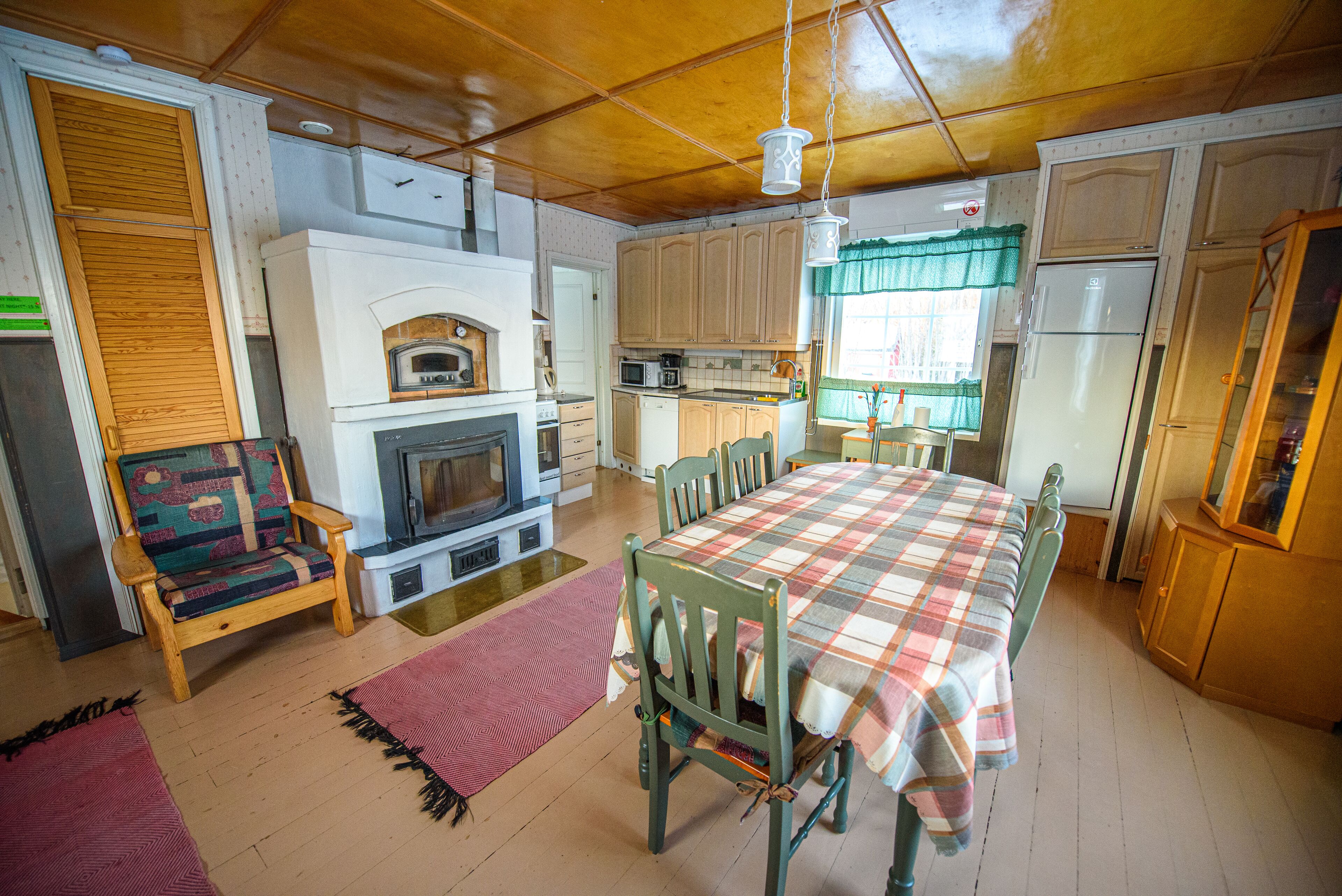 A cozy kitchen with wooden cabinets, a dining table with a plaid tablecloth, and a fireplace.