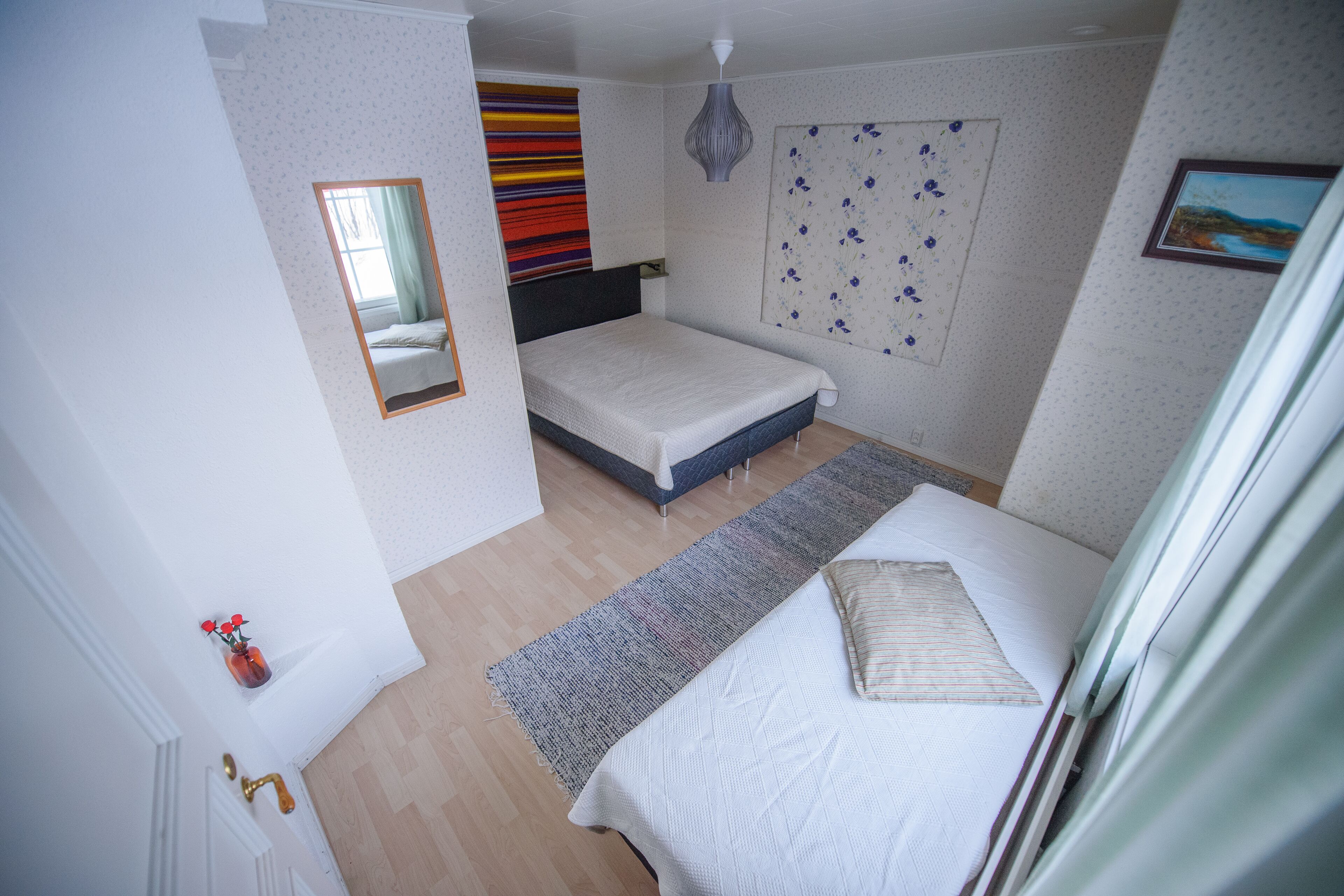 A bedroom with a bed, a bedside table, a mirror, a wall-mounted artwork, and a door with a brass handle.