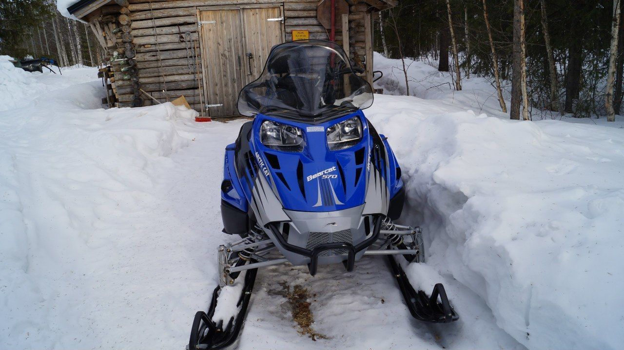 A snowmobile parked in front of a wooden cabin with a snow-covered path.